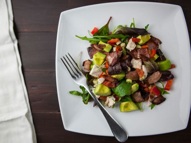 a fresh bacon, avocado, and mixed greens salad served on a square plat image