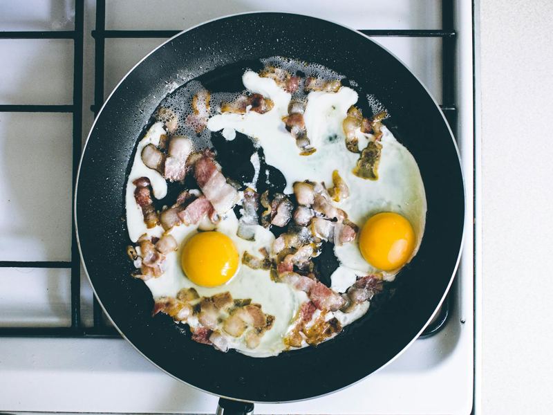 high-angle view of fried eggs and bacon sizzling in a skillet on a gas image